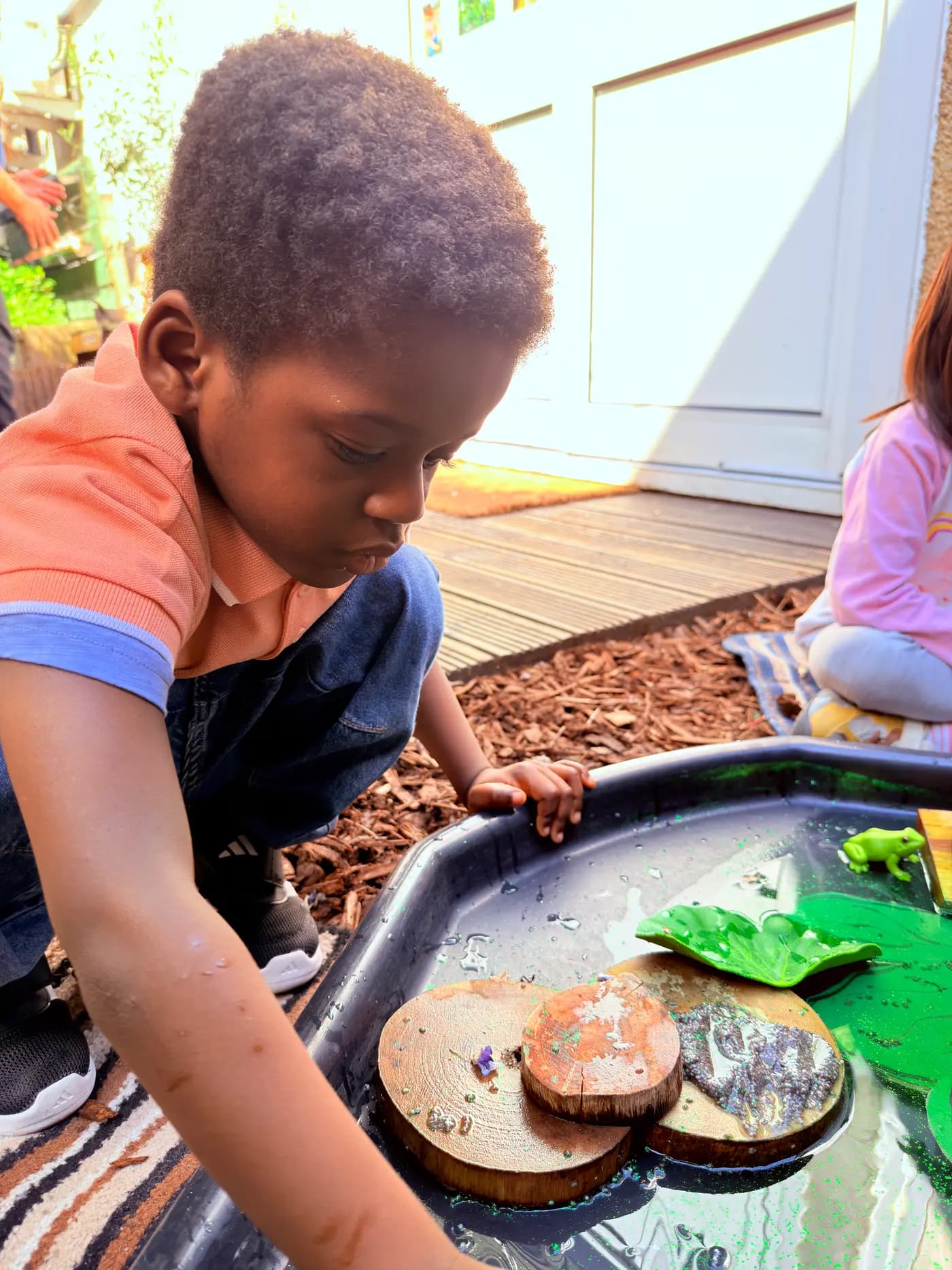 Young child focused on an outdoor wood-and-water sensory tray at Blue Nest Montessori Harrow