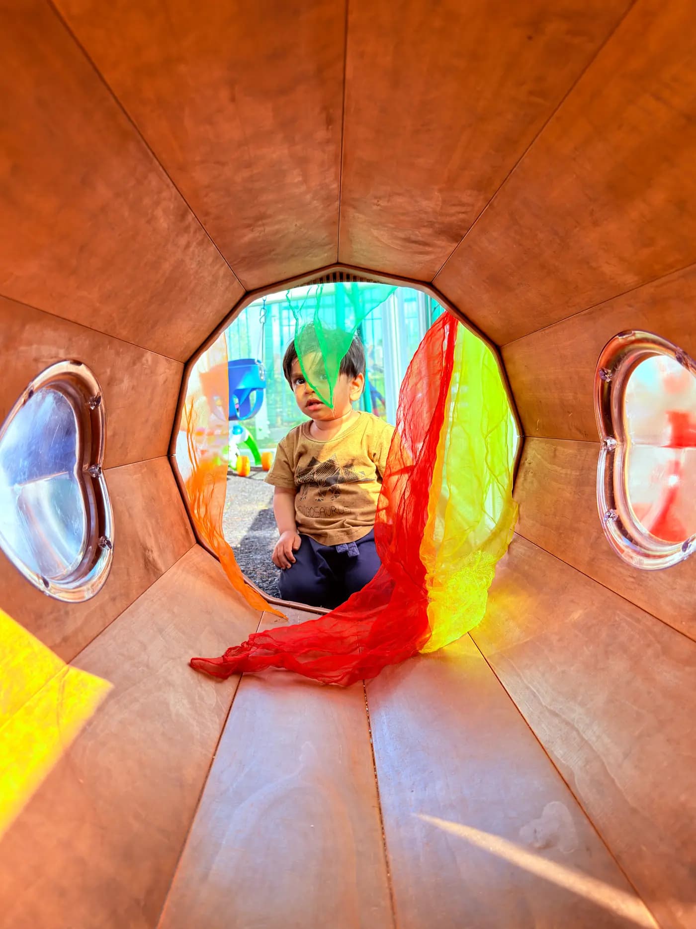 Child playing in an outdoor wooden tunnel at Blue Nest Montessori Harrow